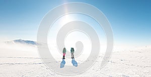 two girls look at the mountains during a winter hike. Two young girls in snowshoes and with backpacks stand on a pass in the