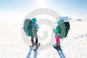 two girls look at the mountains during a winter hike. Two young girls in snowshoes and with backpacks stand on a pass in the
