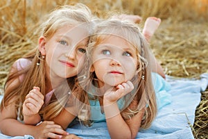 Two girls are lying on a blanket in a wheat field. The sisters are lying on a blanket against the background of rye ears