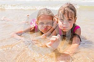 Two girls lying in shallow water and fun pretending faces looking in the frame