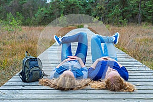 Two girls lying on their backs on wooden path in nature photo