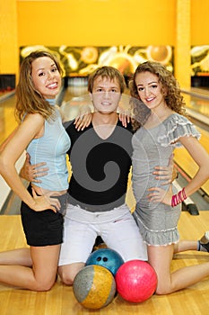 Two girls and man kneel on floor in bowling club