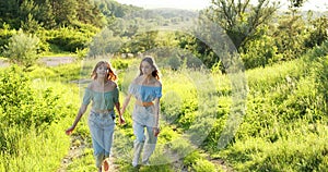 Two girls in nature. Two joyful girls in summer clothes run between the trees, holding hands.