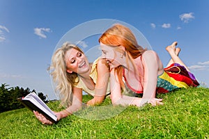 Two girls with notebook on the green grass