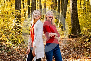 Two girls outdoors enjoying Autumn nature. Portrait of friends women on maple leaves.