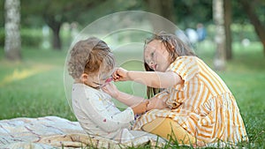 Two girls paint each other's faces at a picnic in the park