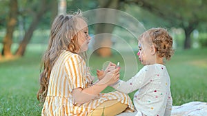 Two girls paint each other's faces at a picnic in the park