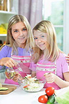 Two girls in pink aprons preparing salad on kitchen table