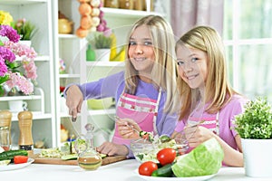 Two girls in pink aprons preparing salad on kitchen table