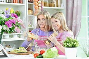 Two girls in pink aprons preparing salad with tablet