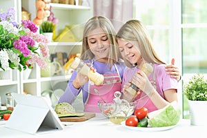 Two girls in pink aprons preparing salad with tablet
