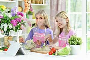 Two girls in pink aprons preparing salad with tablet