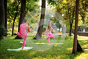 Two girls in the pink sportsuit practice yoga in the park