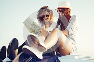 Two girls planning their summer seaside road trip with convertible