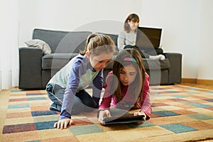 Two girls play in the living room while their mother teleworks