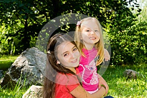 Two girls play in a park on a lawn among enormous stones.