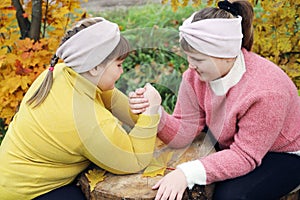 Two girls playing competing in strength of arm-wrestling outdoors in autumn