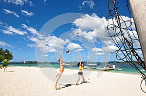 Two girls playing volleyball on white beach