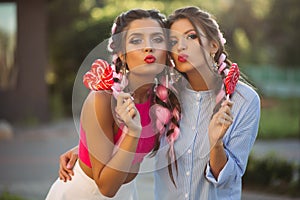 Two girls posing and making duckface with candies heart on stick.