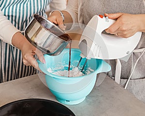 Two girls are preparing homemade marshmallows together. One whips with a mixer, the second pours in jam