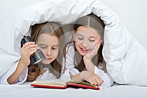 Two girls reading under blanket