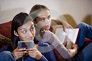 Two girls reclining on sofa look up from texting