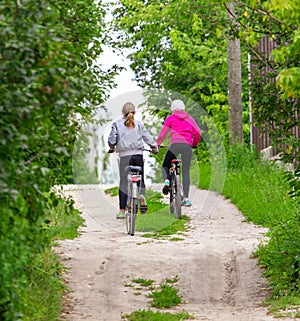 Two girls ride bicycles on a dirt road