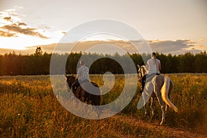 Two girls are riding horses on a dirt road against the background of sunset.