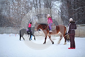 Two girls riding on horses with instructors at the photo