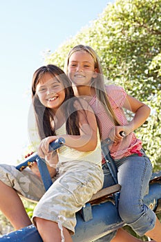 Two Girls Riding On See Saw In Playground