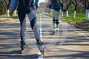 Two girls on roller skates ride along the road next to each other