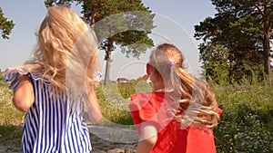 Two girls runaway on green field in summer village. Girl friends running on summer meadow in village back view. Happy