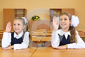 Two girls in school uniform sit at wooden school