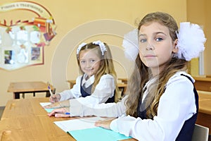 Two girls in school uniform sit at wooden school