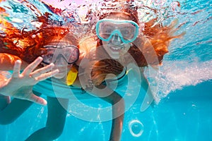 Two girls with scuba mask wave hands dive in pool