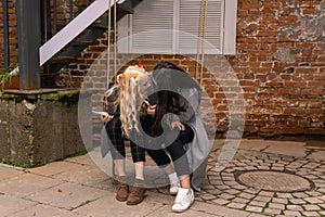 Two girls are secreting about something, sitting on a swing in the courtyard of an old building