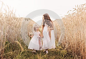 Two girls sister in white dresses walk through a wheat field by the hands