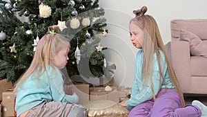 Two girls sisters draw fingers on pillow with sequins sit near Christmas tree.