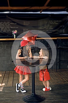 Two girls sisters dressed in retro rock style are standing at cafe table in city courtyard and laughing merrily, blowing out candl