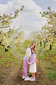 two girls sisters have fun and cuddle in the garden with flowering trees.