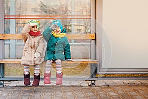 Two girls sit at the bus stop