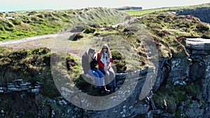 Two girls sit on the edge of the famous Cliffs of Moher in Ireland