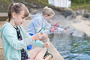 Two Girls Sitting On Harbour Wall Catching Crabs