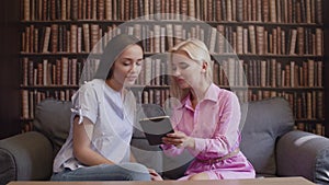 Two girls sit in the library and read a book in electronic form