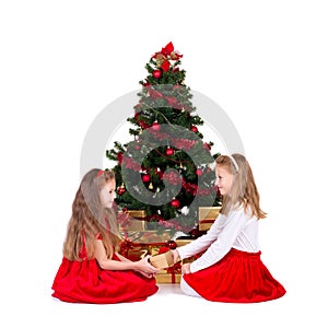 Two girls sit near Christmas tree.