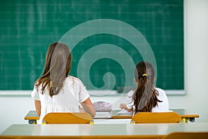 Two girls sit at school desks and look toward blackboard