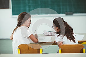 Two girls sit at school desks and look toward blackboard