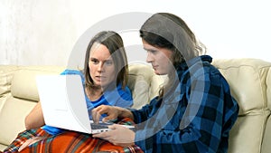 Two girls sit together on the sofa in the living room and using laptop