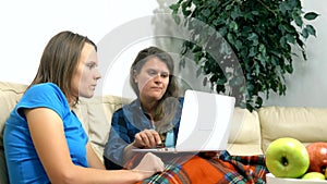 Two girls sit together on the sofa in the living room and using laptop