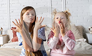 Two girls are sitting on the bed in the bedroom and showing off their new manicure.